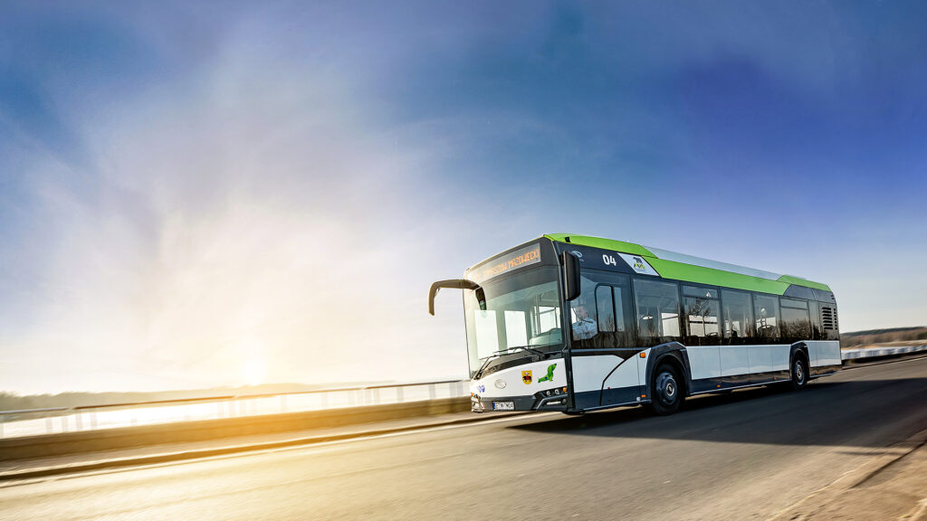 Na zdjęciu widoczny jest hybrydowy autobus MZK w ruchu, z charakterystycznym logo spółki